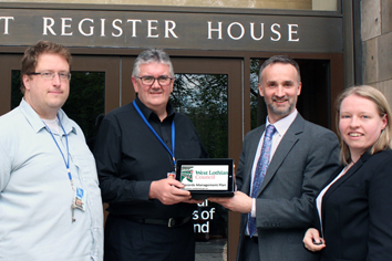Photograph of Carol Dunn and Roberto Riaviz handing over the Records Management Plan of West Lothian Council and West Lothian Licensing Board to Dr Hugh Hagan and Robert Fotheringham of the NRS PRSA Assessment Team